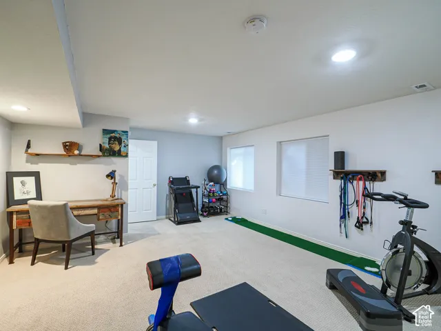 Recessed lighting illuminates this versatile space featuring light-toned carpeting and two windows with blinds