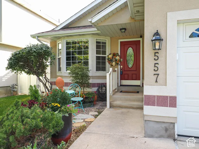 Red entry door with oval glass insert, bay window with grid pattern, exterior wall-mounted lantern, white garage door, and concrete walkway