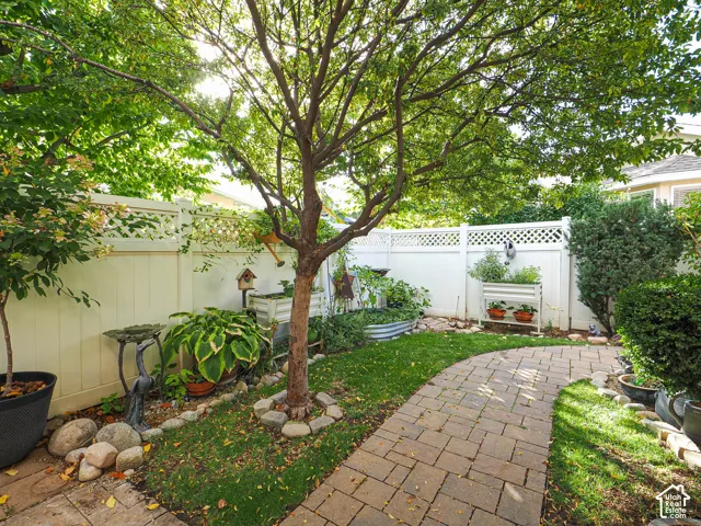 Manicured lawn with mature trees, paver pathway, white privacy fencing with lattice accents, and raised garden beds