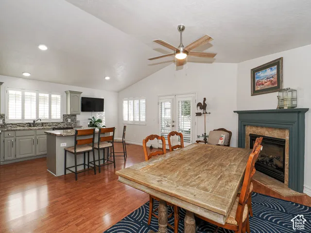 Vaulted ceiling with a ceiling fan, fireplace with a painted wood mantel, wood-finish flooring, kitchen island with seating, and white window shutters