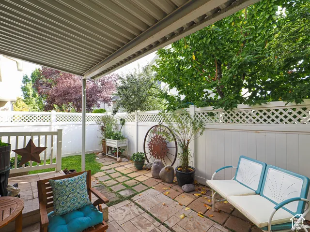 Patio with a slatted overhead covering, stone paver flooring, and white lattice fencing