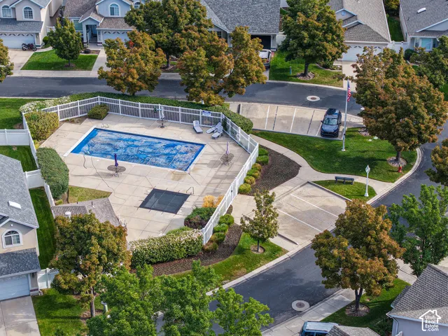 Fenced community pool with a surrounding paved patio, landscaping, and adjacent parking