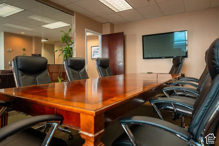 Spacious meeting room featuring a polished wood-finish conference table, wall-mounted display, recessed ceiling lights, and a full-height glass partition