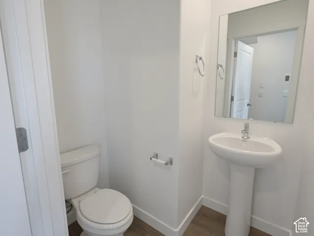 Pedestal sink, wall-mounted mirror, modern toilet, and wood-finish flooring