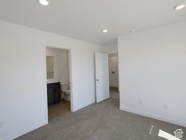 Plush carpeting, recessed lighting, and crisp white walls, with an adjacent bathroom featuring wood-finish flooring and a dark wood-finish vanity