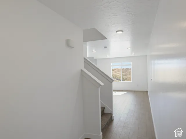 Recessed lighting, wood-finish flooring, carpeted staircase, white railing, and a large window