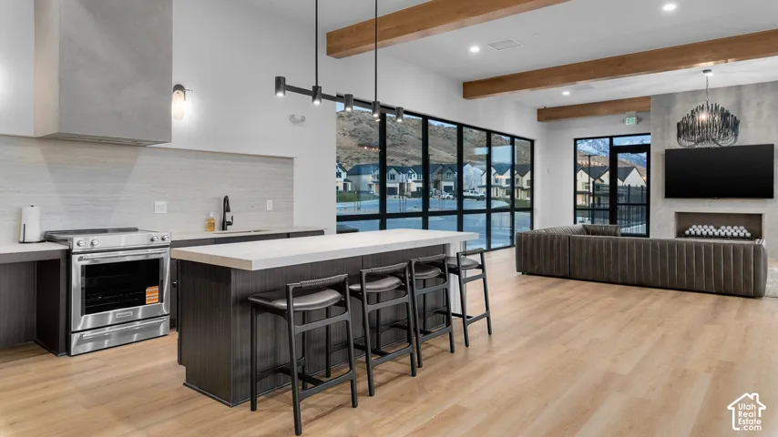 Open-concept interior featuring wood-finish flooring, a kitchen island with seating, full-height glass windows, exposed ceiling beams, and a built-in linear fireplace