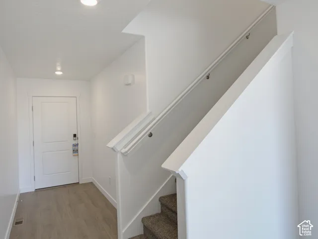 Entryway featuring wood-finish flooring, a paneled door, recessed lighting, and a carpeted staircase with a white railing