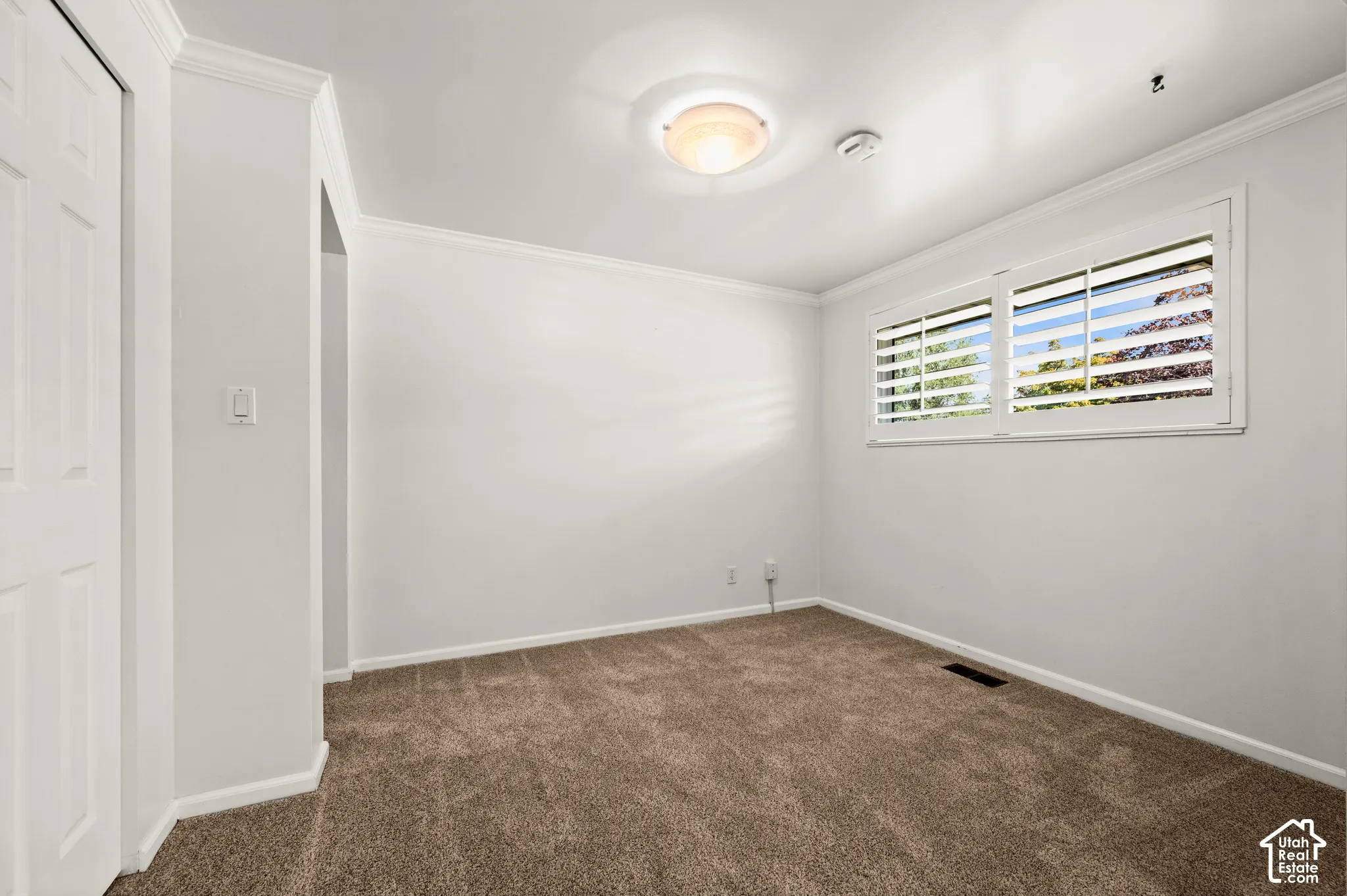 Wall-to-wall carpeting, window with interior shutters, ceiling-mounted light fixture, and crown molding