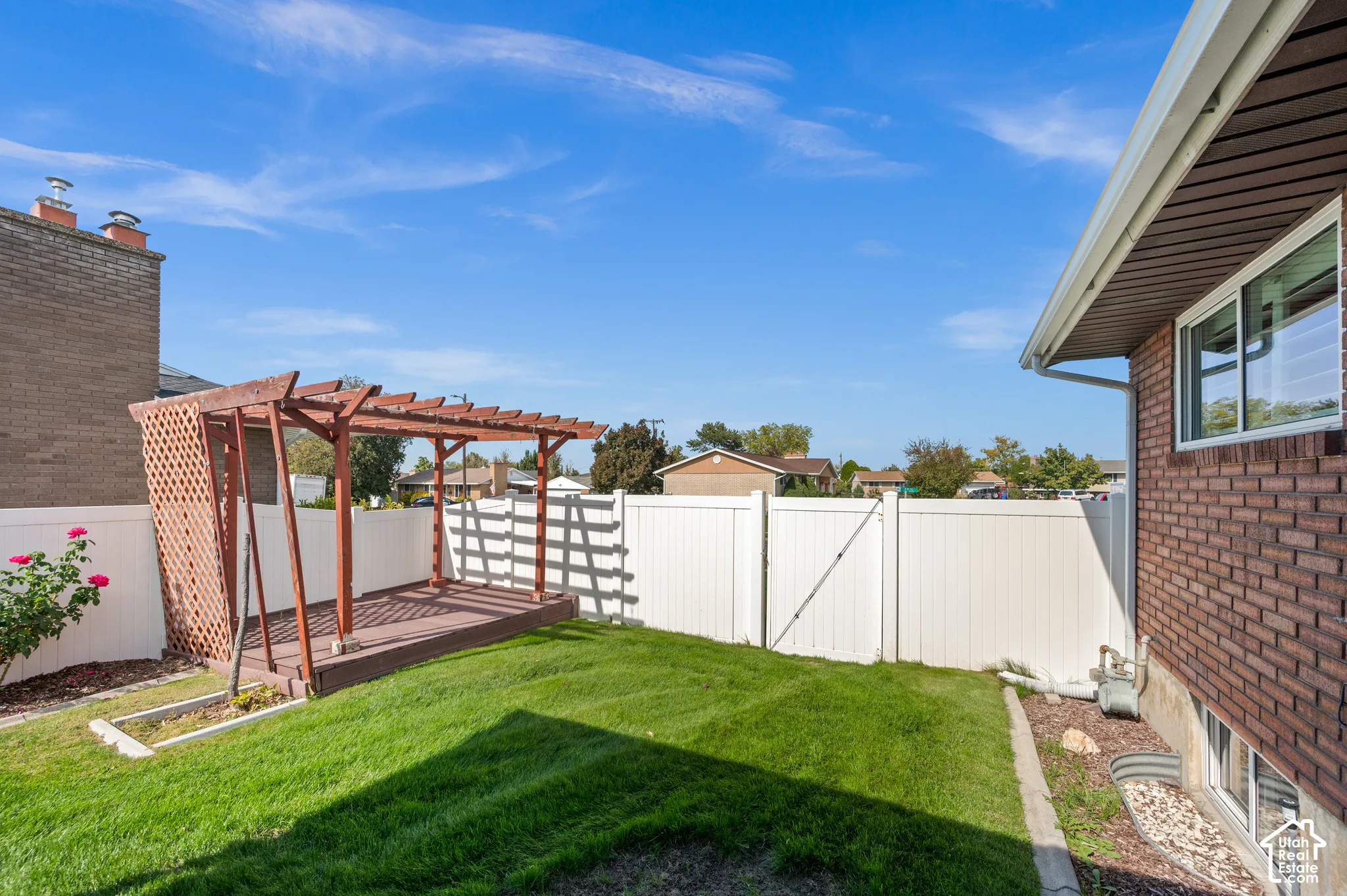 Manicured lawn with a wood pergola and a white privacy fence