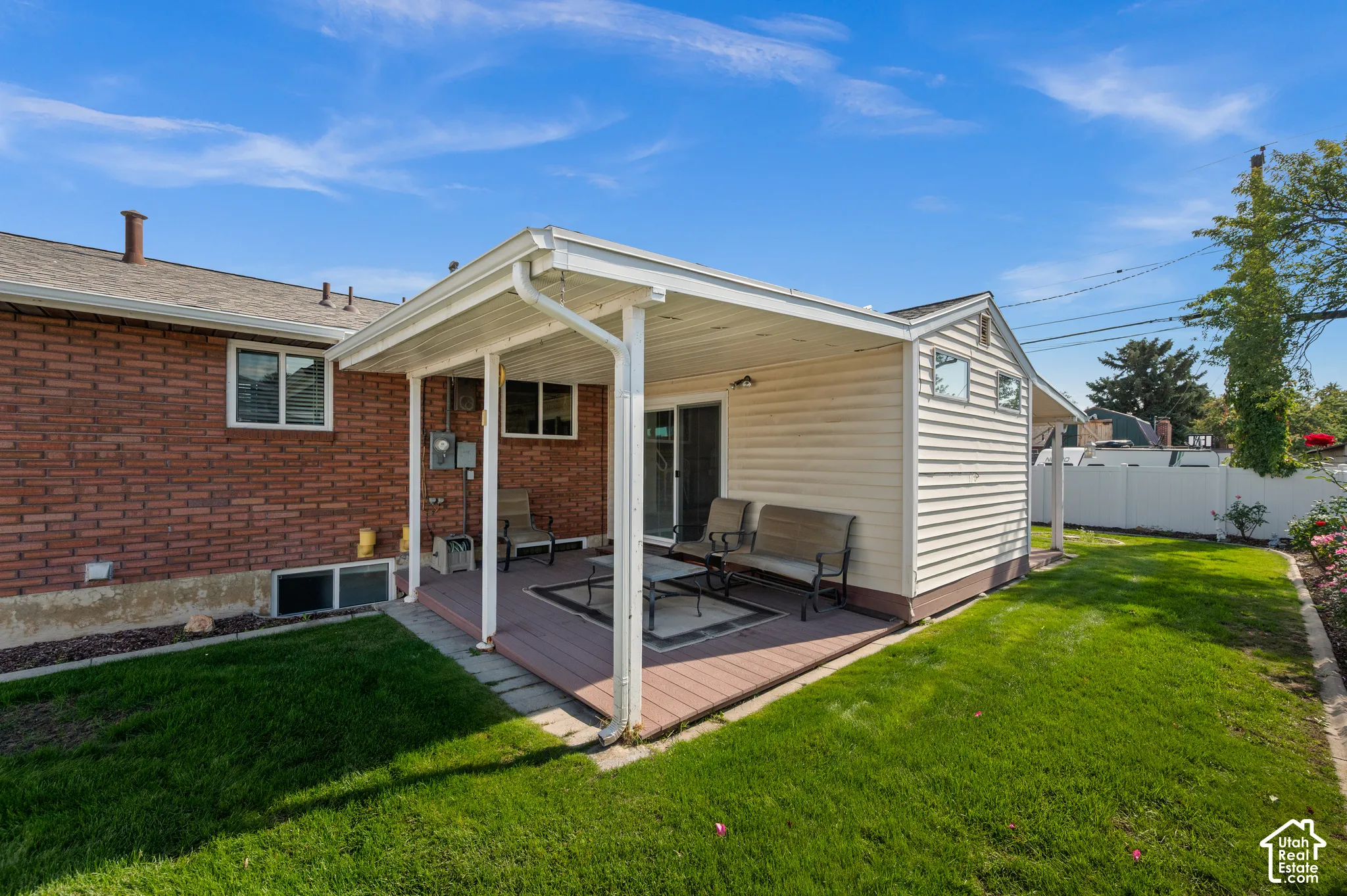 Covered deck with a wood-finish floor and white structural supports, featuring a sliding glass door entry