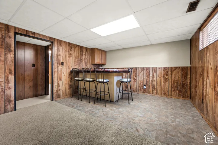 Interior space featuring wood-finish paneling, a built-in bar with cabinetry, and mixed flooring with carpeting and tile