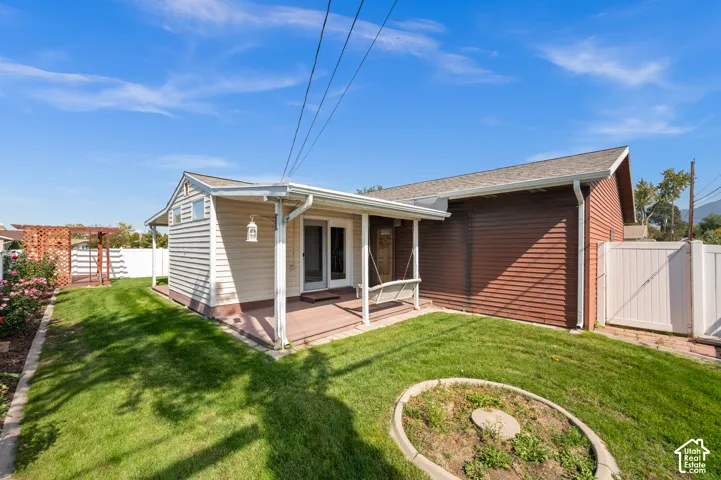 Expansive backyard featuring a covered patio, manicured lawn, white vinyl fencing, and a decorative trellis