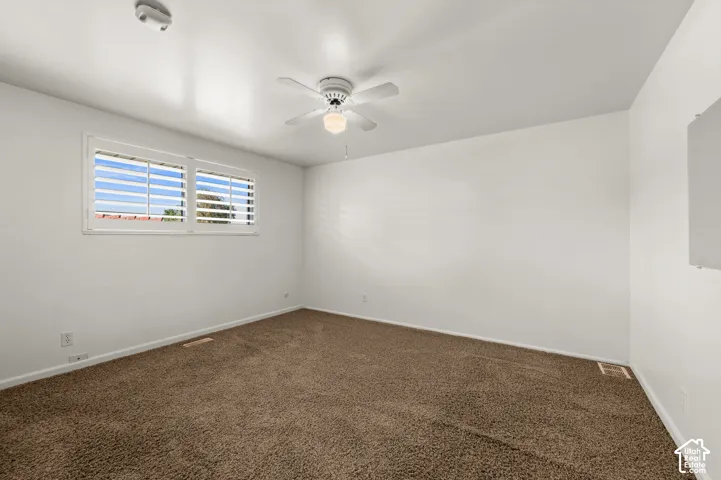 Room featuring soft brown carpeting, white walls, a white ceiling fan with integrated lighting, and a window with white louvered shutters