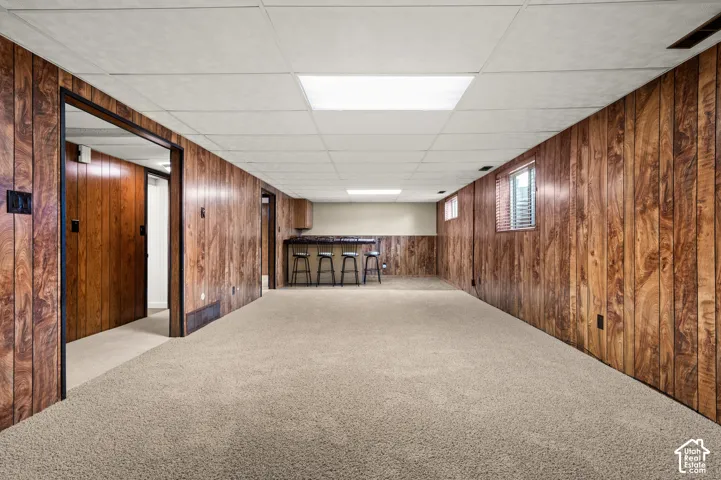 Finished lower level featuring wood-look paneling, drop ceiling with integrated lighting, carpeted flooring, and a built-in bar area with a countertop