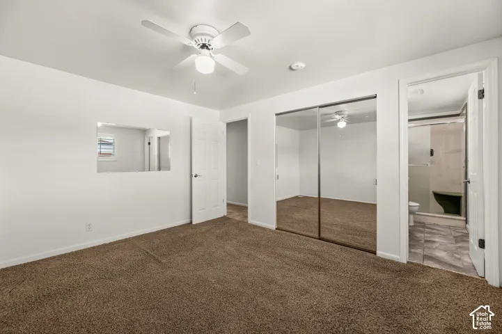 Brown carpet flooring, white walls, white ceiling fan with integrated lighting, mirrored sliding closet doors, and a paneled white door
