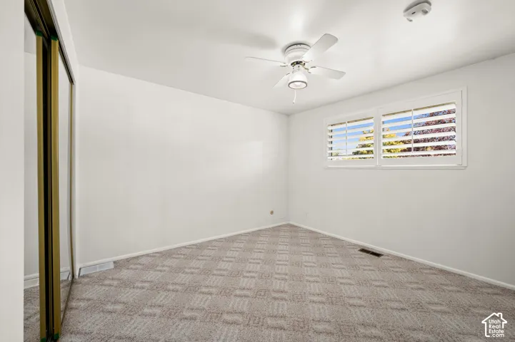 Mirrored closet doors, patterned carpet flooring, ceiling fan with integrated lighting, and plantation shutters