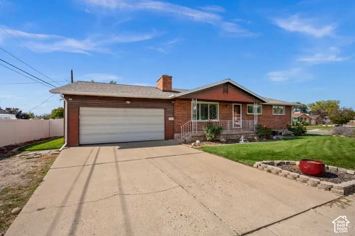 Brick facade home with an attached garage, concrete driveway, and front lawn