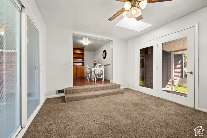 Carpeted flooring, white walls, ceiling fan with integrated lighting, glass sliding door, and double French doors