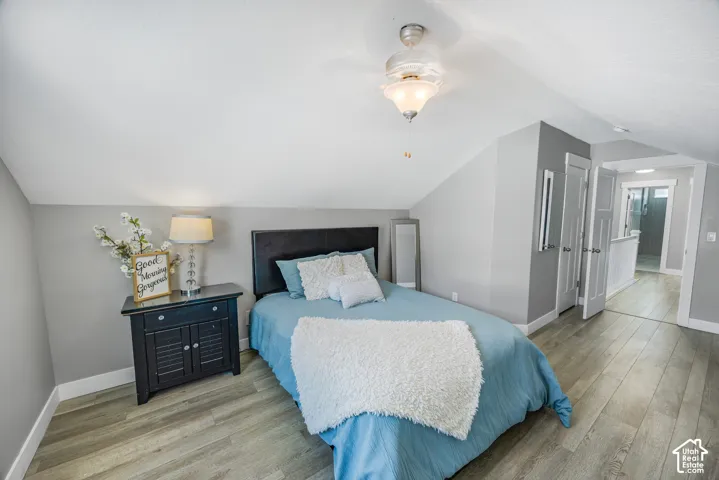Sloped ceiling room featuring wood-finish flooring, light gray walls, a ceiling fan with integrated lighting, and white trim