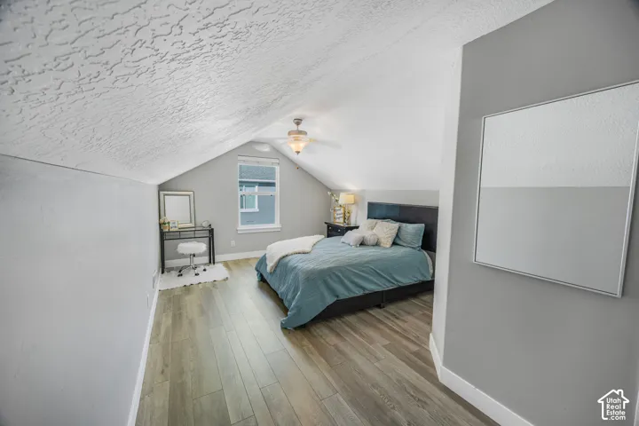 Pitched ceiling with textured finish, wood-finish flooring, recessed window, and ceiling fan with integrated lighting
