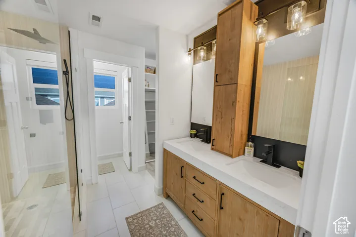 Double vanity with wood-finish cabinetry, integrated sinks, black fixtures, and a glass-enclosed shower