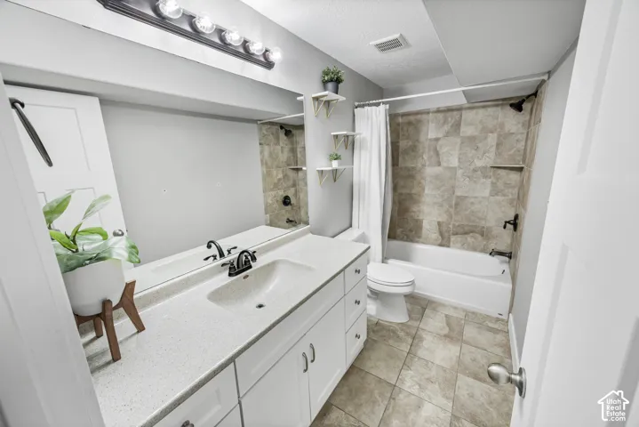 Modern bathroom featuring a white vanity with dual-sink configuration and quartz countertop, chrome faucetry, tile-surround shower/tub combination with glass enclosure, ceramic tile flooring, and recessed ceiling lighting