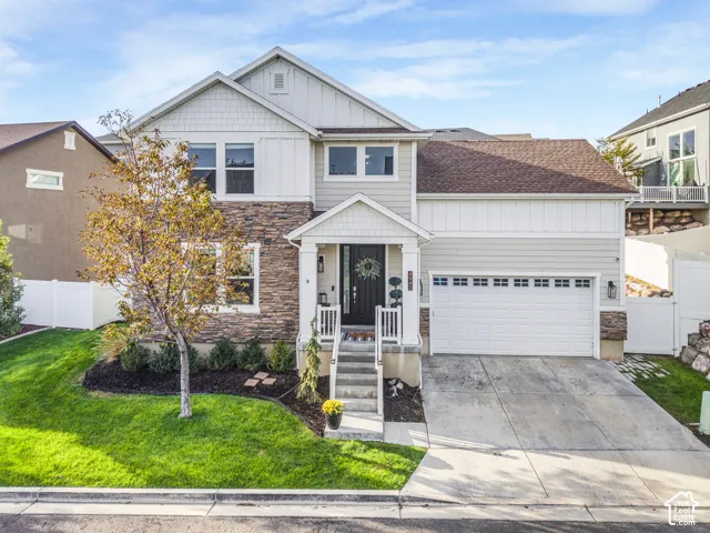 Contemporary exterior featuring a stone and siding facade, covered entry, attached garage, concrete driveway, and a manicured lawn