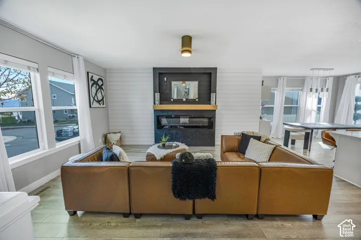 Living space featuring wood-finish flooring, a contemporary fireplace with a dark surround and wood mantel, shiplap accent wall, and multiple windows