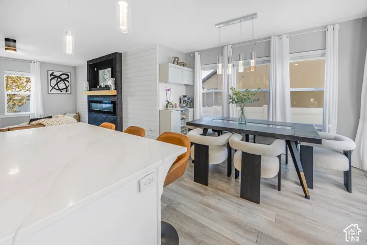 Expansive white countertop island, wood-finish flooring, built-in fireplace with black surround, shiplap accent wall, and multiple windows with white trim