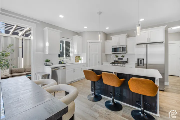 Kitchen featuring white cabinetry, stainless steel appliances, a center island with seating, pendant lighting, and wood-finish flooring