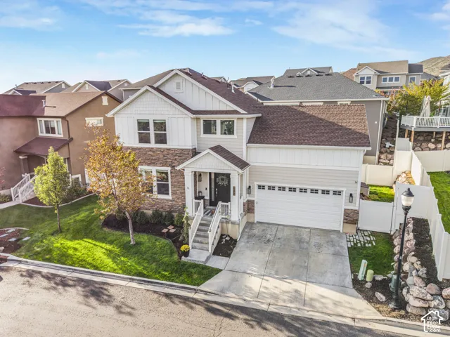 Two-story residence featuring a two-car garage, stone and siding exterior, front porch with railings, and established landscaping