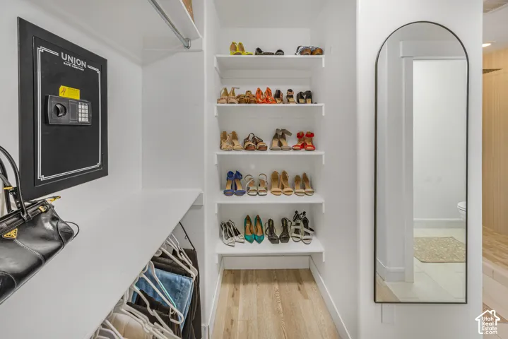 Built-in wall safe, white shelving system, clothes hanging rod, arched full-length mirror, wood-finish flooring