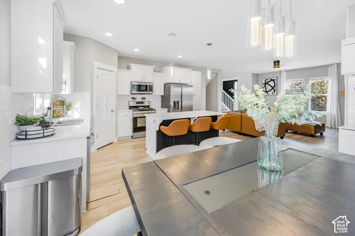 Open-concept living space featuring wood-finish flooring, white cabinetry, a kitchen island with seating, stainless steel appliances, and a modern chandelier