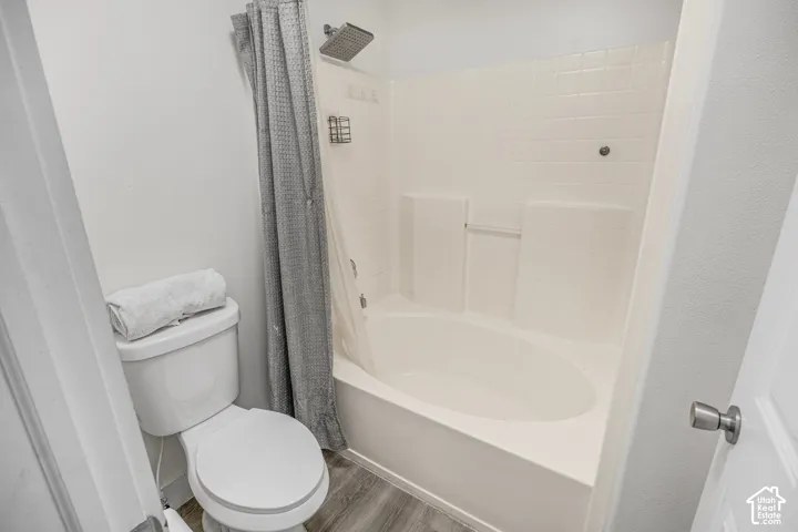 Full bathtub with white tile surround, rainfall shower head, and wood-finish flooring