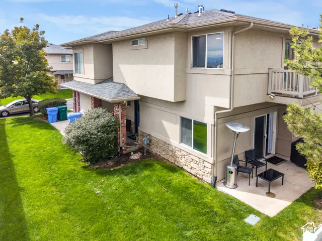 Stucco exterior with stone veneer accents, upper-level balcony, ground-level patio, and sliding glass door