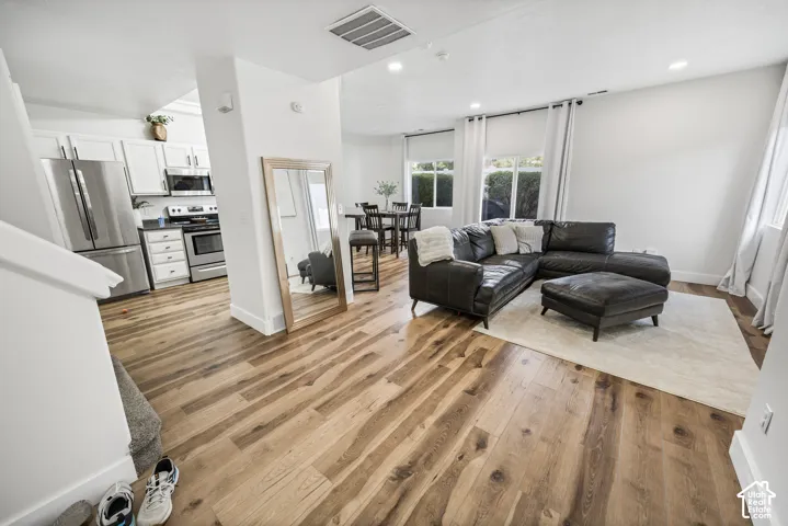 Open-concept living area with wood-finish flooring, white walls, recessed lighting, and a kitchen featuring stainless steel appliances and white cabinetry