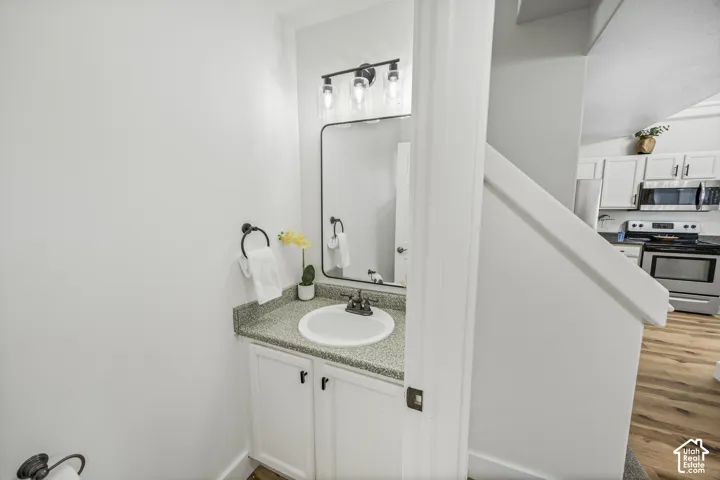 White vanity with a round basin sink and speckled countertop, illuminated by a three-light fixture above a rectangular mirror