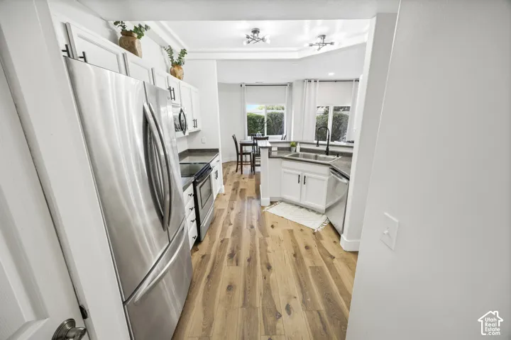 Modern kitchen featuring stainless steel appliances, wood-finish flooring, white cabinetry, dark countertops, and a double basin sink with a matte black faucet