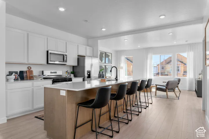 Bright kitchen featuring white cabinetry, stainless steel appliances, a center island with seating, and wood-finish flooring