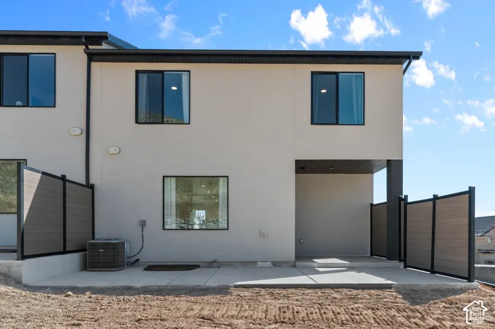 Stucco exterior with black-framed windows, ground-level concrete patio, covered outdoor living space, and privacy fencing