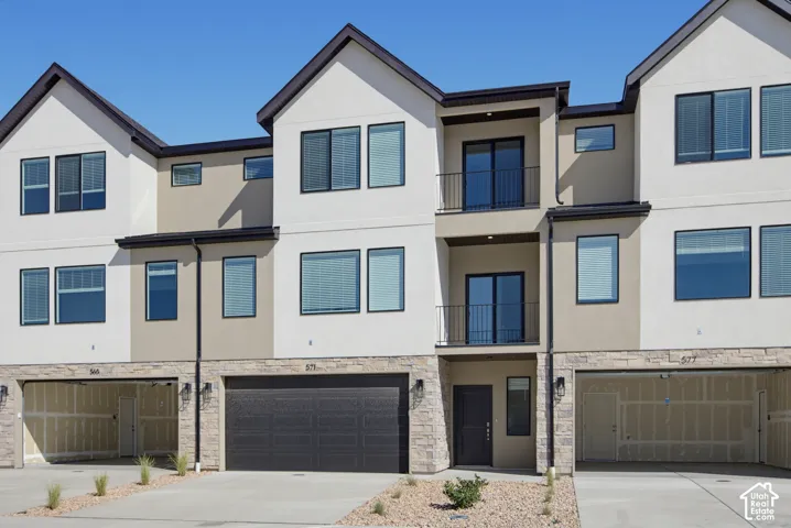 Three-story exterior with stucco and stone-finish siding, multiple balconies with metal railings, dark-framed windows, and an attached two-car garage