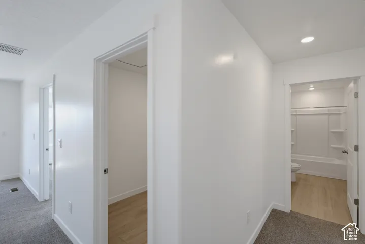 Recessed lighting, light wood-finish flooring, white walls, white trim, and a built-in shower/tub combination
