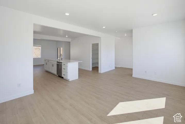 Open-concept living area with wood-finish flooring, recessed lighting, and a white kitchen island featuring an integrated sink, stainless-steel dishwasher, and ample cabinetry