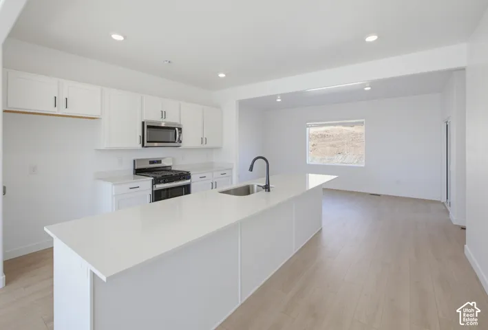 Kitchen featuring white cabinetry, stainless steel microwave, gas range, recessed lighting, and an expansive island with a sink and black faucet