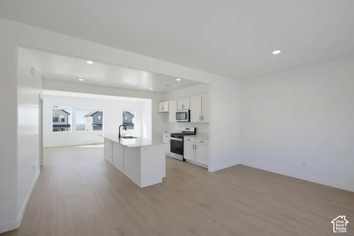Open-concept living area with light wood-finish flooring, recessed lighting, and white walls