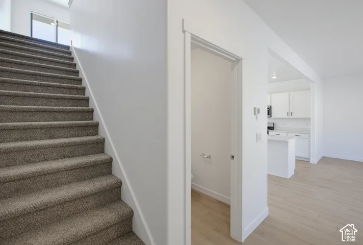 Carpeted staircase, white interior walls, wood-finish flooring, and a kitchen with white cabinetry and an island