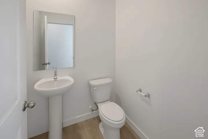 Pedestal sink with chrome faucet, mirror, toilet, and wood-finish flooring