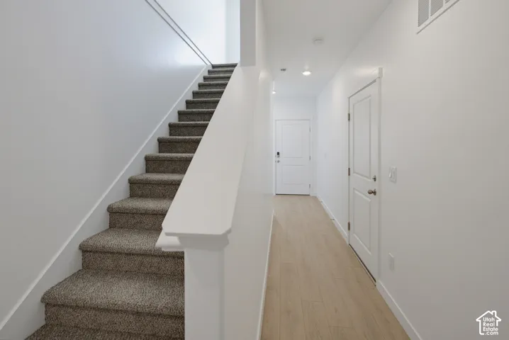 Carpeted staircase with white baluster and handrail, light wood-finish flooring, white walls, and recessed lighting