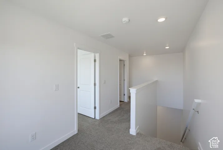 Carpeted hallway with white walls, recessed ceiling lighting, and solid white doors